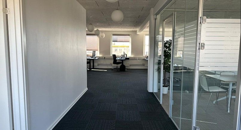 Moderne kontor med hvide vægge, gulve med mørk grå linoleum og glasvægge. To stole og to skriveborde med computere samt et