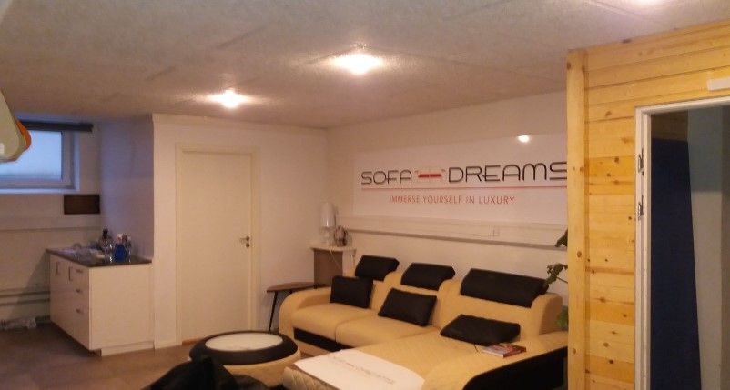 Et luksuriøst og moderne interiør med Sofa Dreams-mærke på væggen og en hvid sofa med sorte puder