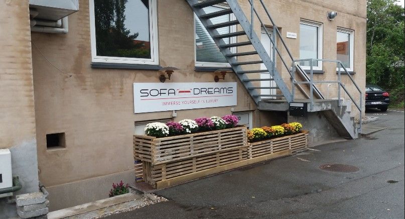 Sofa Dreams-butik med lyse blomster i trækasser foran, samt trappe og et køretøj parkeret udenfor