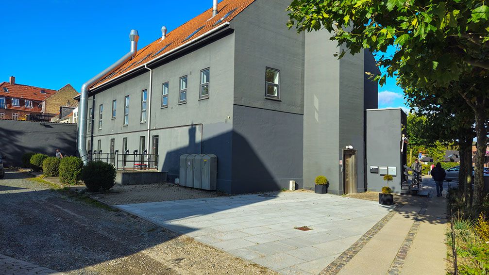 Lejlighedsbygning med flere lejligheder og parkeringsplads i forgrunden og en mand i baggrunden på en gangbro