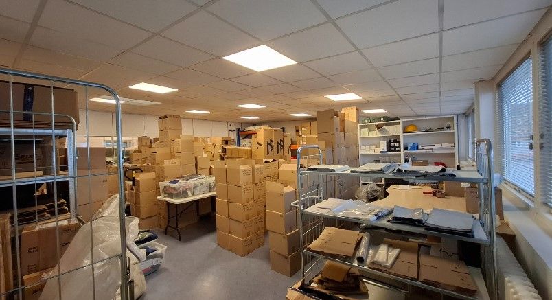 Lager med mange kartoner og kasser samt diverse emballagemateriale og bøsser, hvilket antyder et lager med mange varer.