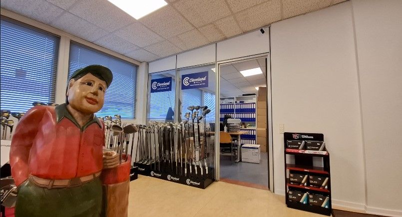 Golfbutik med mange golfkøller og en stor golfstatue i forgrunden og flere golfkøller i baggrunden.