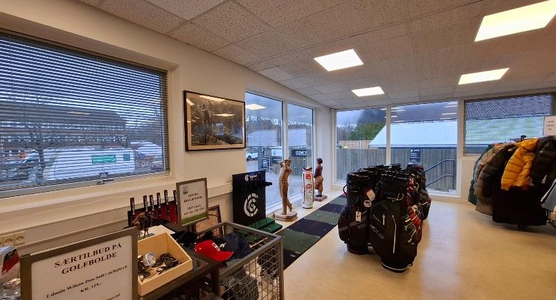 Inde i en golfforretning er der store vinduer, lysekroner, sportsudstyr, tøj, kasser og hylder med diverse artikler og kunder