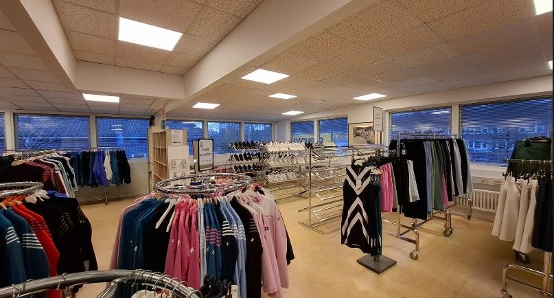 Klædeskab med mange tøj på hængere, forskellige farver og mærker, hvide vægge og gulv, vinduer med udsigt til byen, og