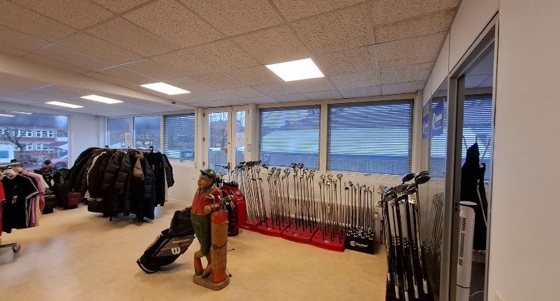Inde i en sportsbutik er der udstille golfkøller, en mandsstatue, og klædeskab med tøj samt vinduer med udsigt til gaden og