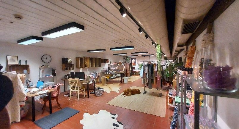 Et rum med flere lysekroner og et gulv med røde klinkefliser. Der er flere borde med computere, og en hund sover på gulvet.