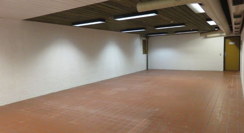 Lokaler til leje i Vallensbæk med 157 kvm, hvid væg, gulv med røde fliser, højt loft med lysekroner og rør.