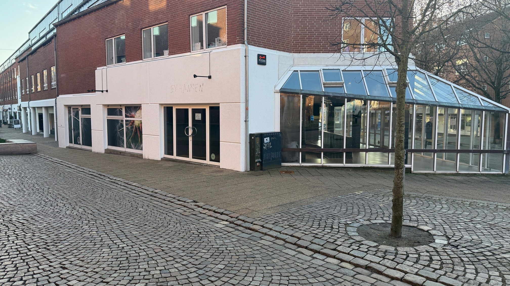 Kolding Sundheds Oasen med glasparti og terrasse på torvet i Kolding med træer og betonbrolæg