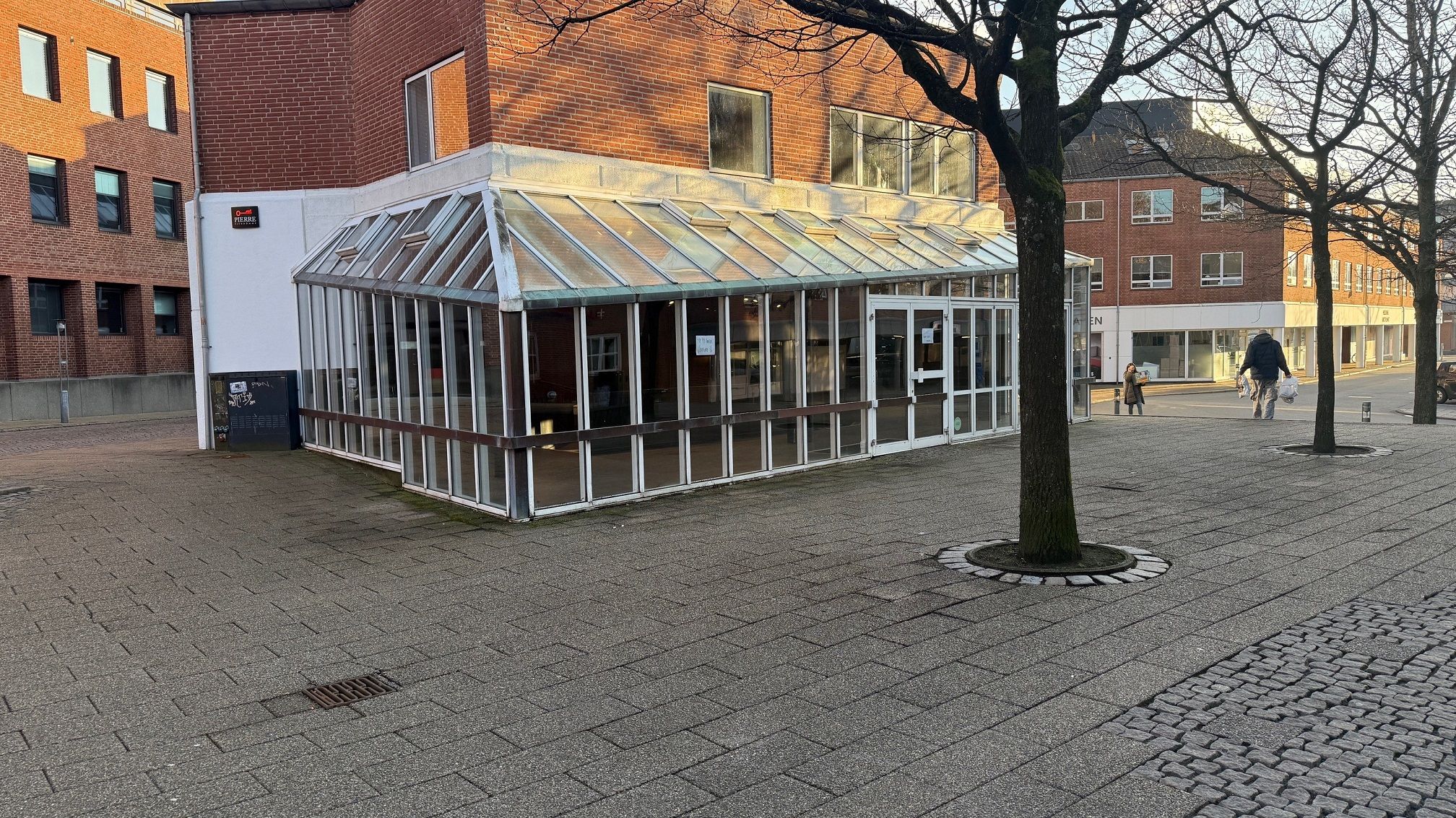 Glasdækket café på Torvet i Kolding med stolpe og salgsskilt - Bredgade og Ny Vestergade i baggrunden - Mennesker med