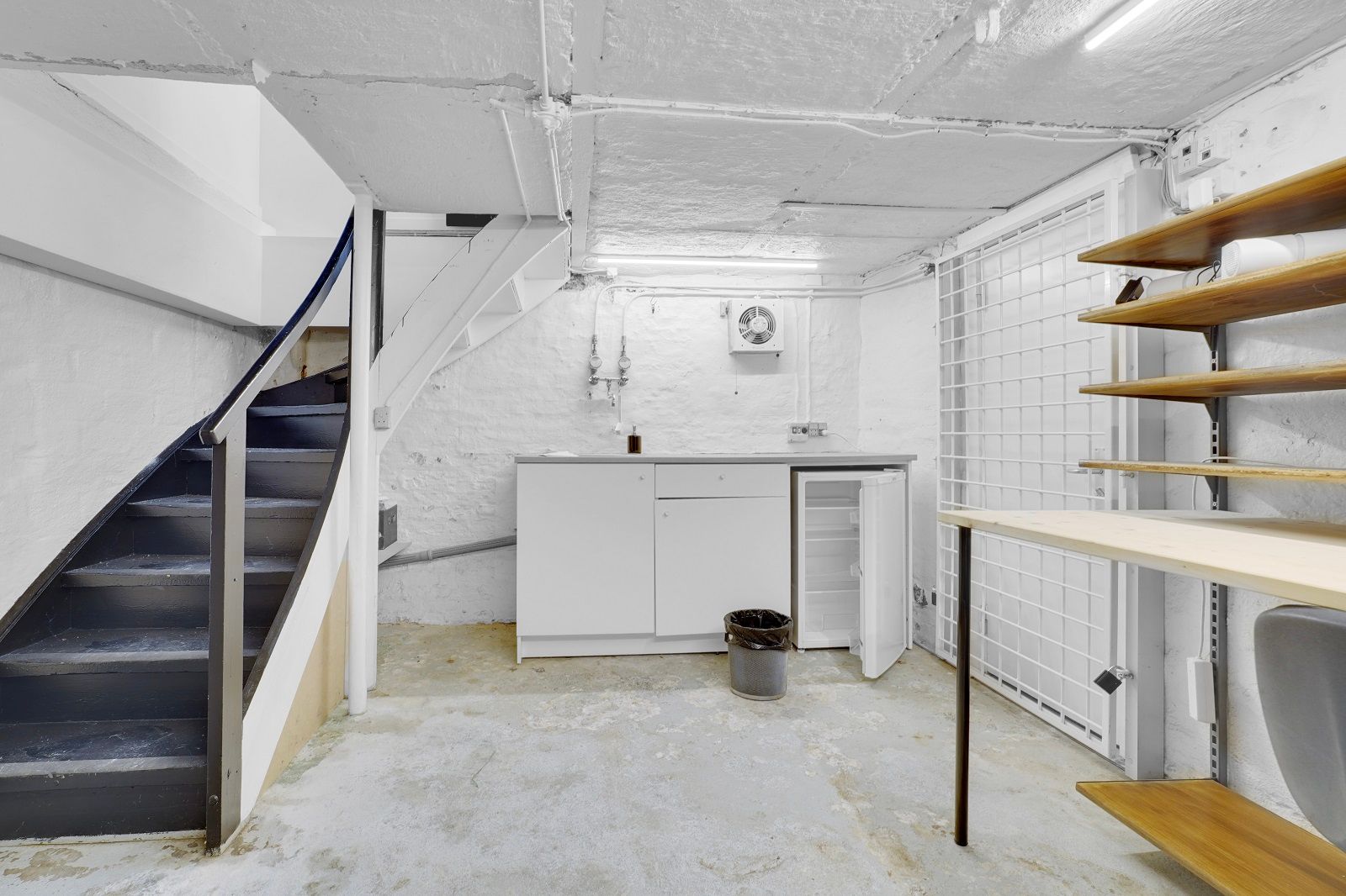 En stor hvid og ren loftsrum med hvidt køkken og en lukket køleskab i kabinetsrækken. Til højre er der en stor, hvid, lukket