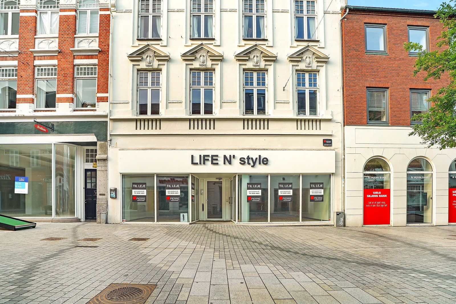 En moderne, hvid facade til en butik med "LIFE N' style" på en gågade. Butikken har glasruder og åbne døre. En rød skilt med