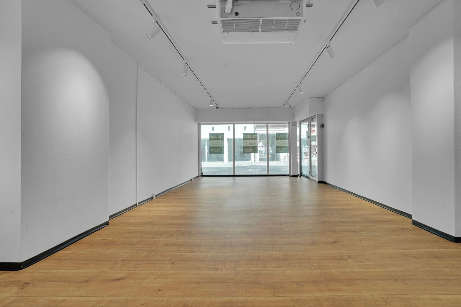 Butik med glasdøre og hvide vægge, trægulv, reklameskilte, luftkanaler og spots i loftet
