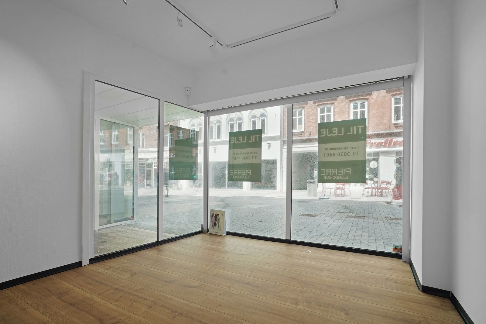 En moderne butik med store vinduer og glasdøre i Esbjerg. Udenfor er røde stole og et torg med gågade. Butikken har