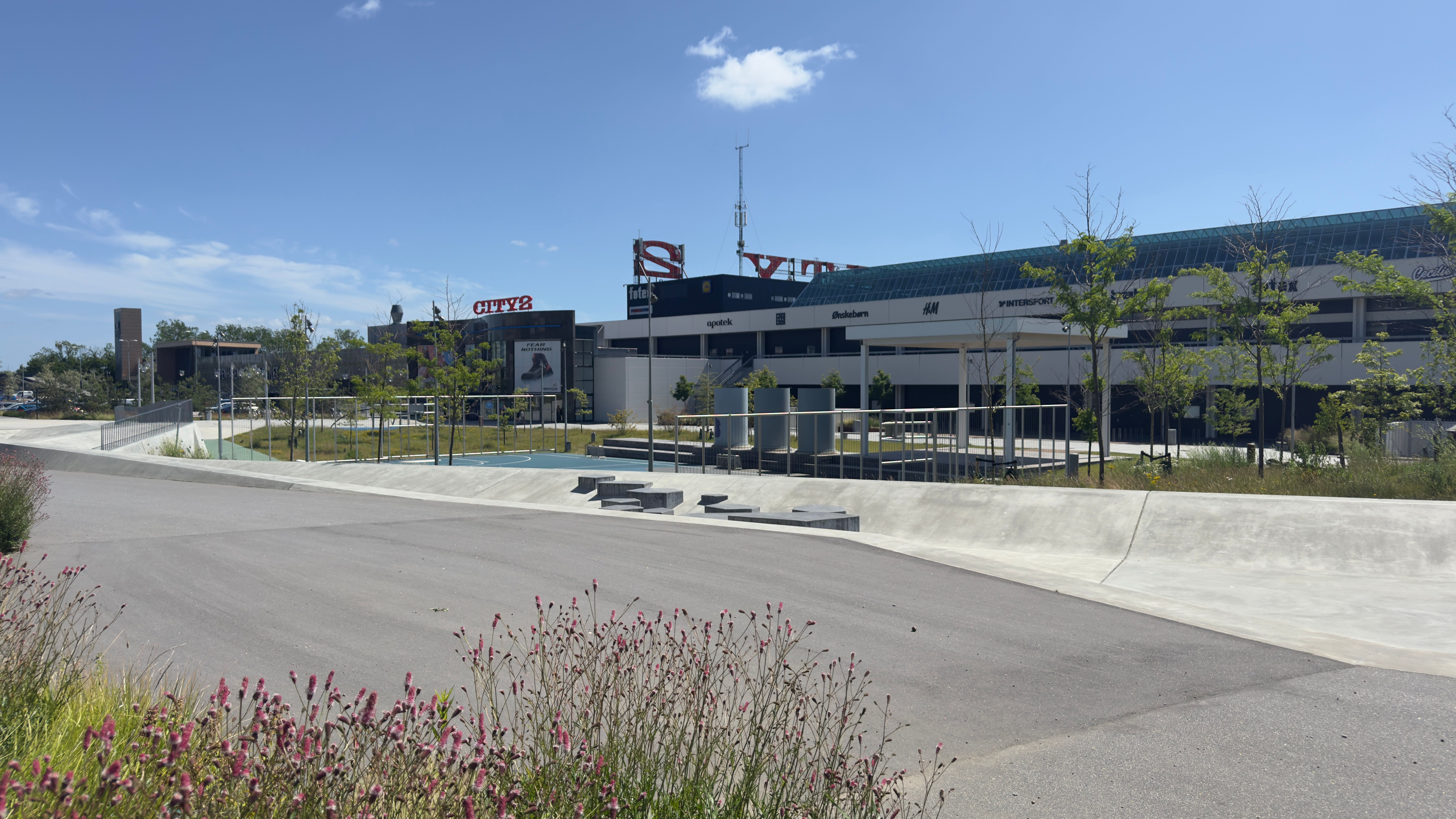 City2 shoppingcenter med butikker og parkeringsplads og skulpturer med blomster langs vejen