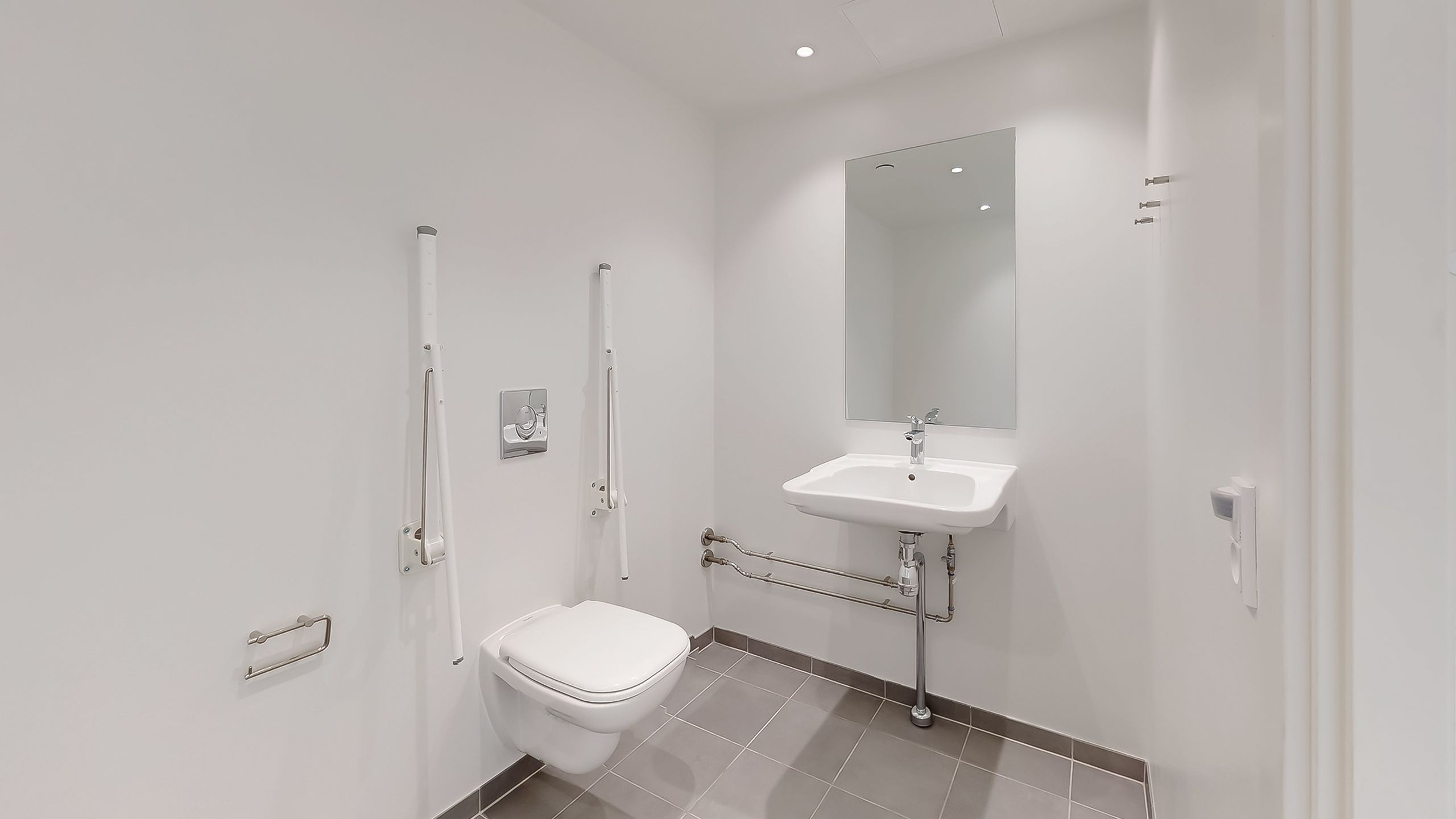 En hvid toilet i et luksuriøst badeværelse med en hvidt tøjskab og håndtag og en hvidt højtryksblæser i et hjørne