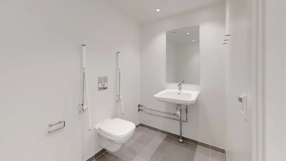 En hvid toilet i et luksuriøst badeværelse med en hvidt tøjskab og håndtag og en hvidt højtryksblæser i et hjørne