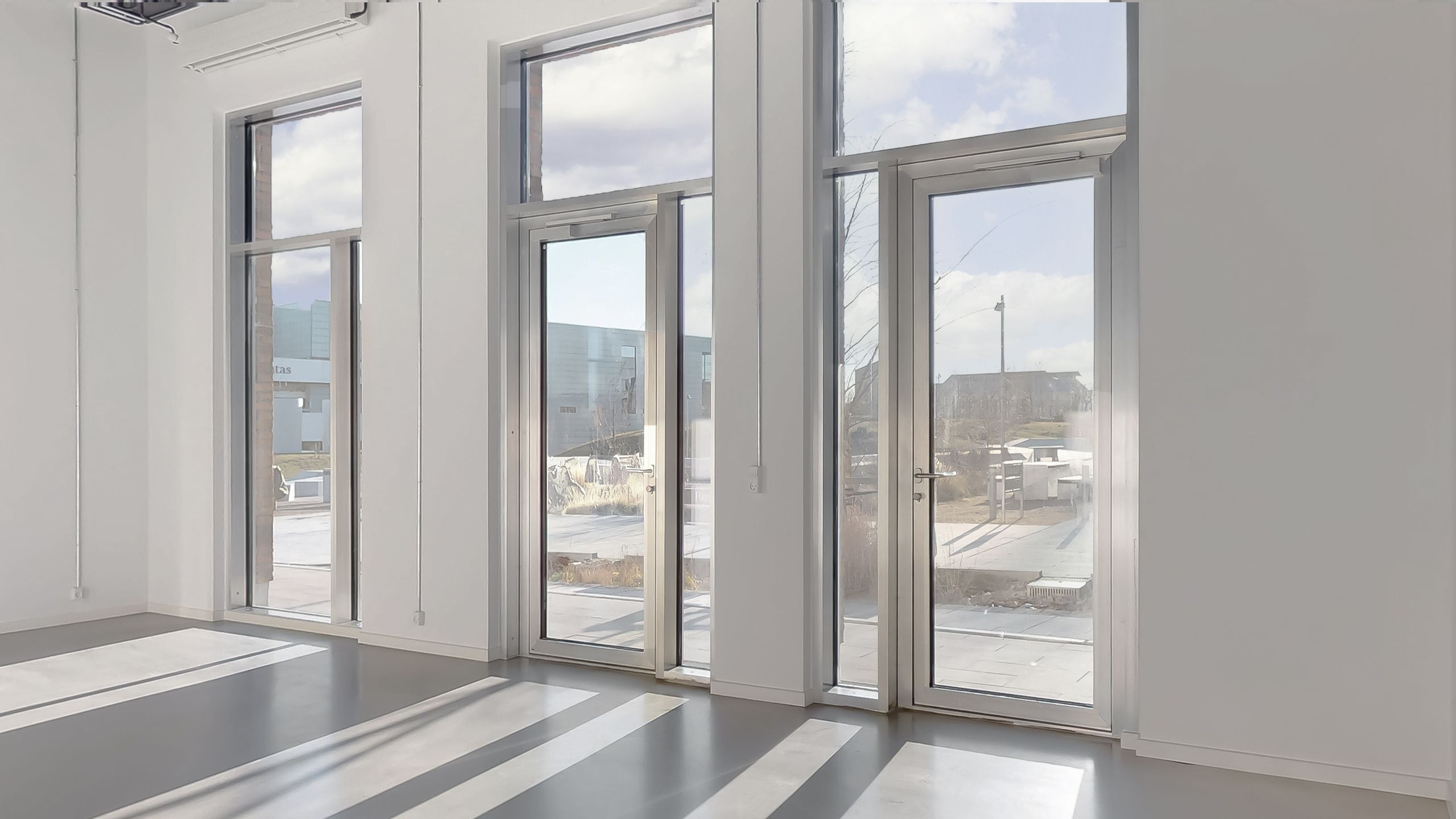 Glassdøre med refleksioner i et tomt kontor med hvide vægge og gulv. Et sammensat udendørs område med en bygning og søjler