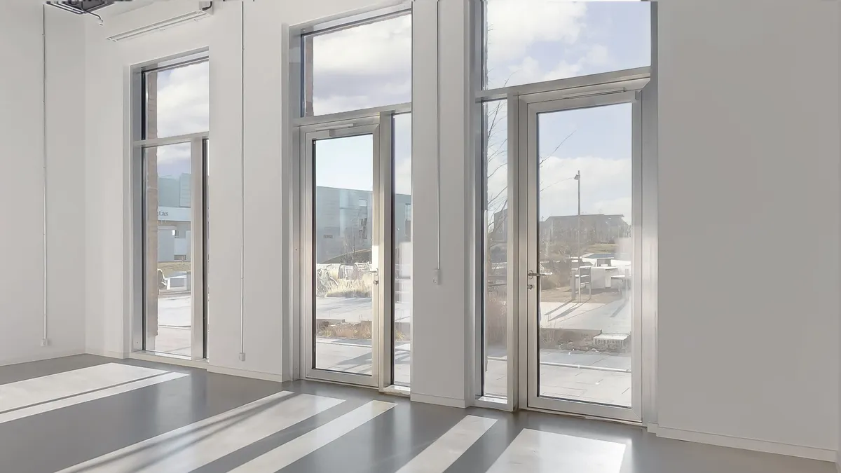 Glassdøre med refleksioner i et tomt kontor med hvide vægge og gulv. Et sammensat udendørs område med en bygning og søjler