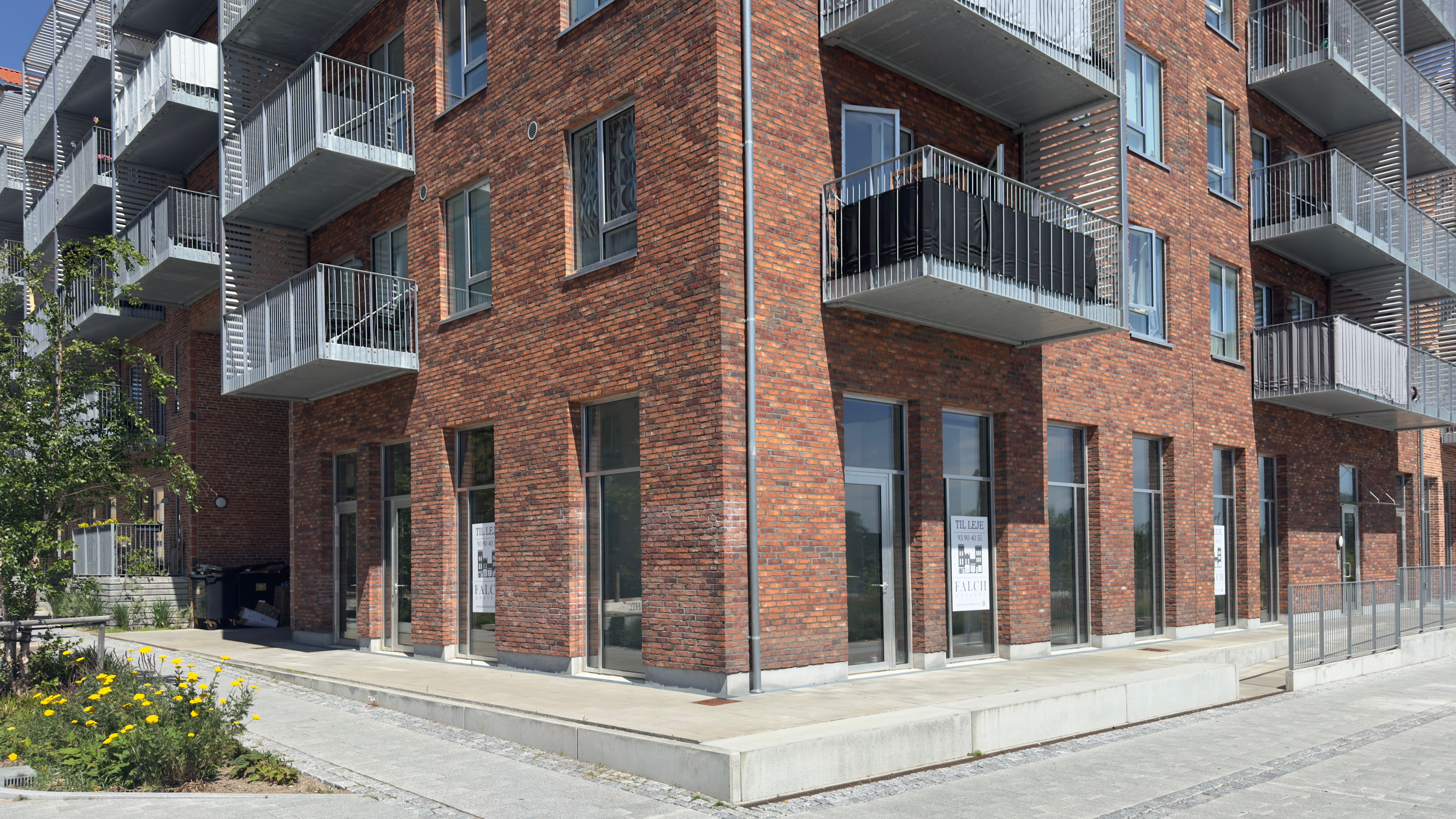 Rød teglstensbygning med glasvinduer og fire balkoner på højre side og to balkoner på venstre side. To glasdøre med skilte.