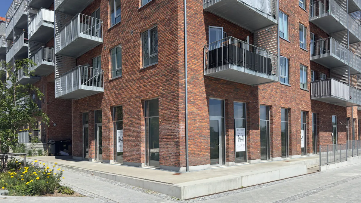 Rød teglstensbygning med glasvinduer og fire balkoner på højre side og to balkoner på venstre side. To glasdøre med skilte.