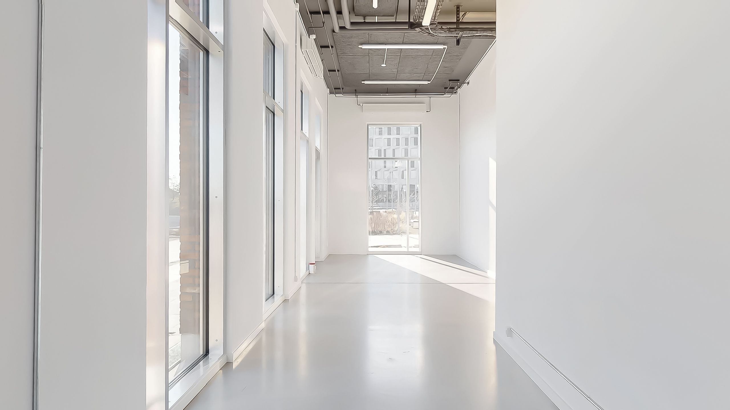 En lukket gang med glasvinduer og hvide vægge med lyse gulvbelægning og ingen møbler