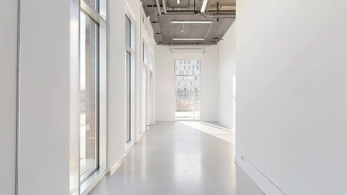 En lukket gang med glasvinduer og hvide vægge med lyse gulvbelægning og ingen møbler