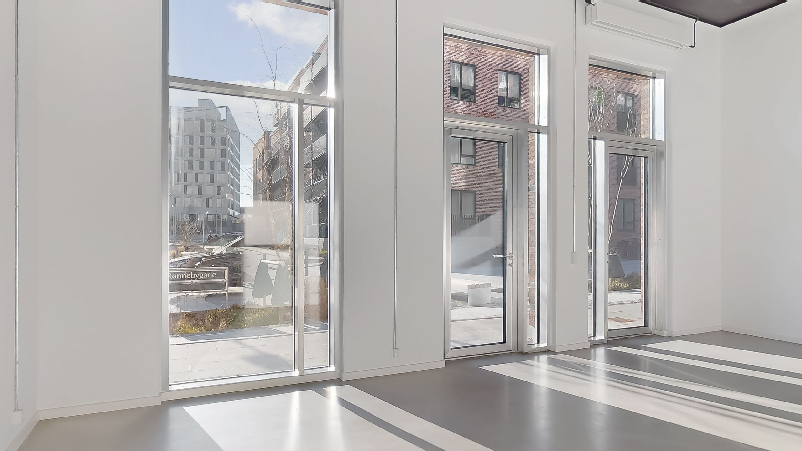 Et glasdækket lokale med to store glasdøre og vinduer, der vender ud mod en bygning og en parkeringsplads