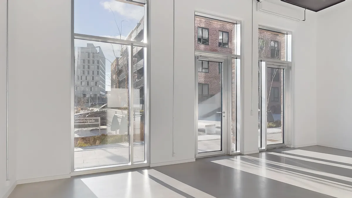 Et glasdækket lokale med to store glasdøre og vinduer, der vender ud mod en bygning og en parkeringsplads