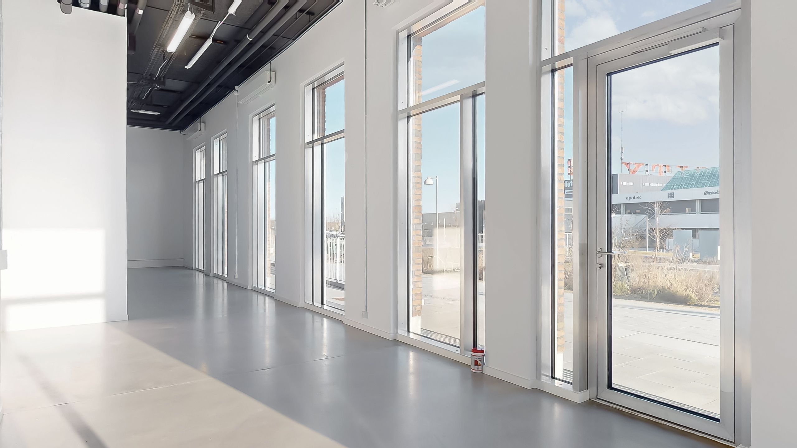 En stor, lys og åben erhvervslokal med hvide vægge, vinduer og gulv og en dør med håndtag til udgangen