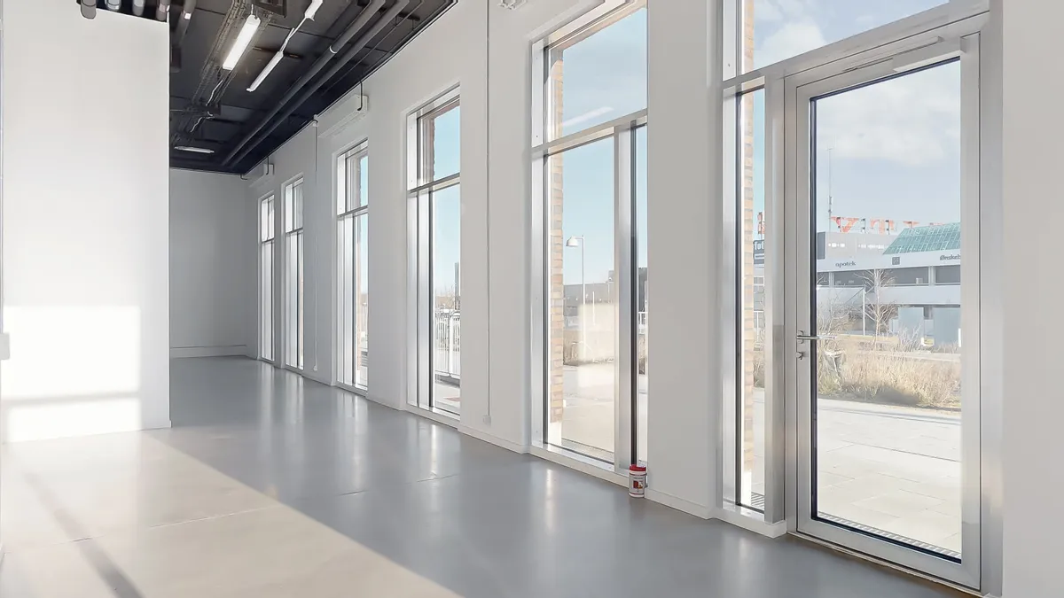 En stor, lys og åben erhvervslokal med hvide vægge, vinduer og gulv og en dør med håndtag til udgangen