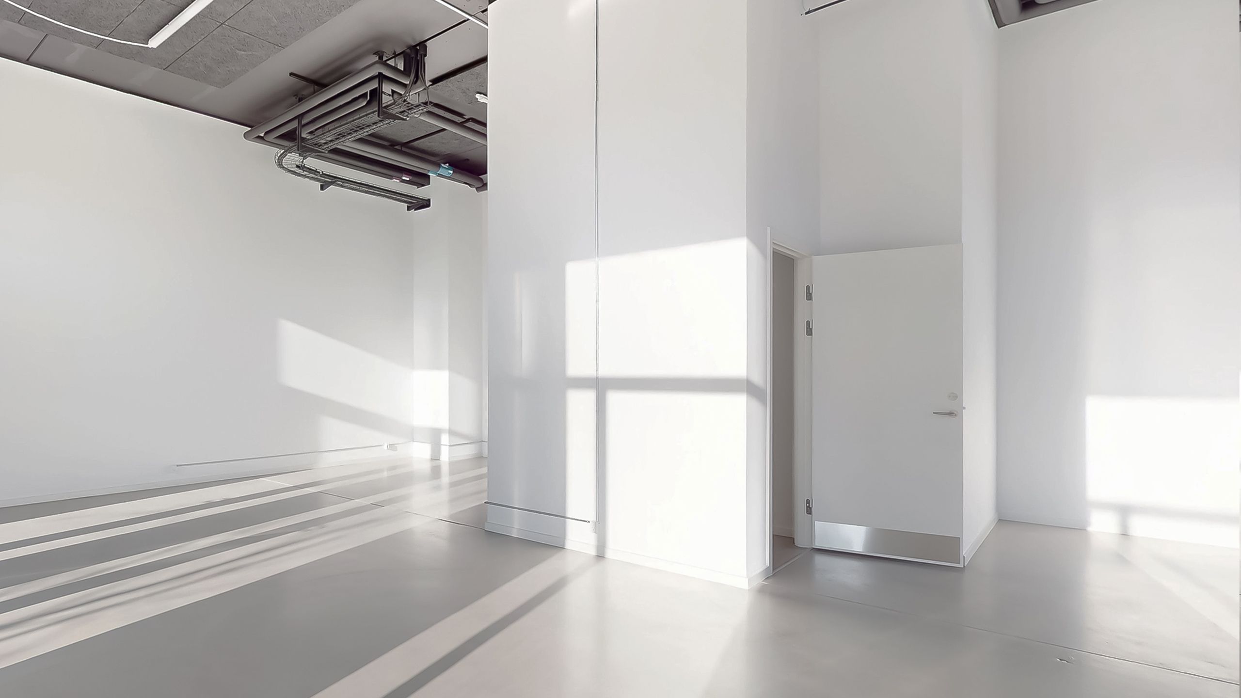 Et minimalistisk rum med hvide vægge og gulv, åbne døre og en lyse skygger på gulvet fra vinduet