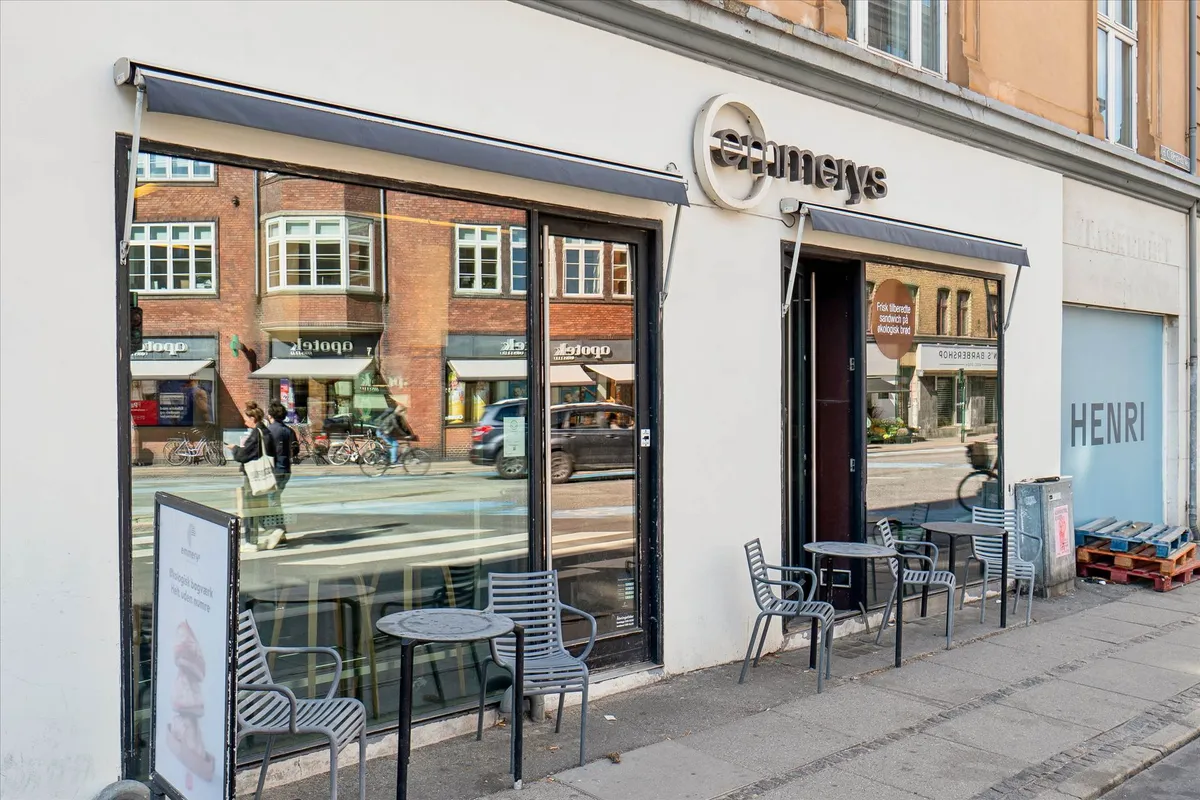Glass facade of an outdoor cafe with a sign reading "EMMAEYS" and reflections of bicycles and cars on the street