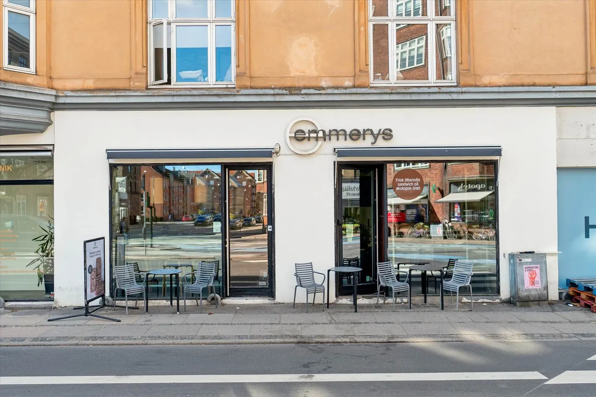 Forretningsentré med teksten "emmerys" og flere bord og stole på fortovet og glasdøre og vinduer