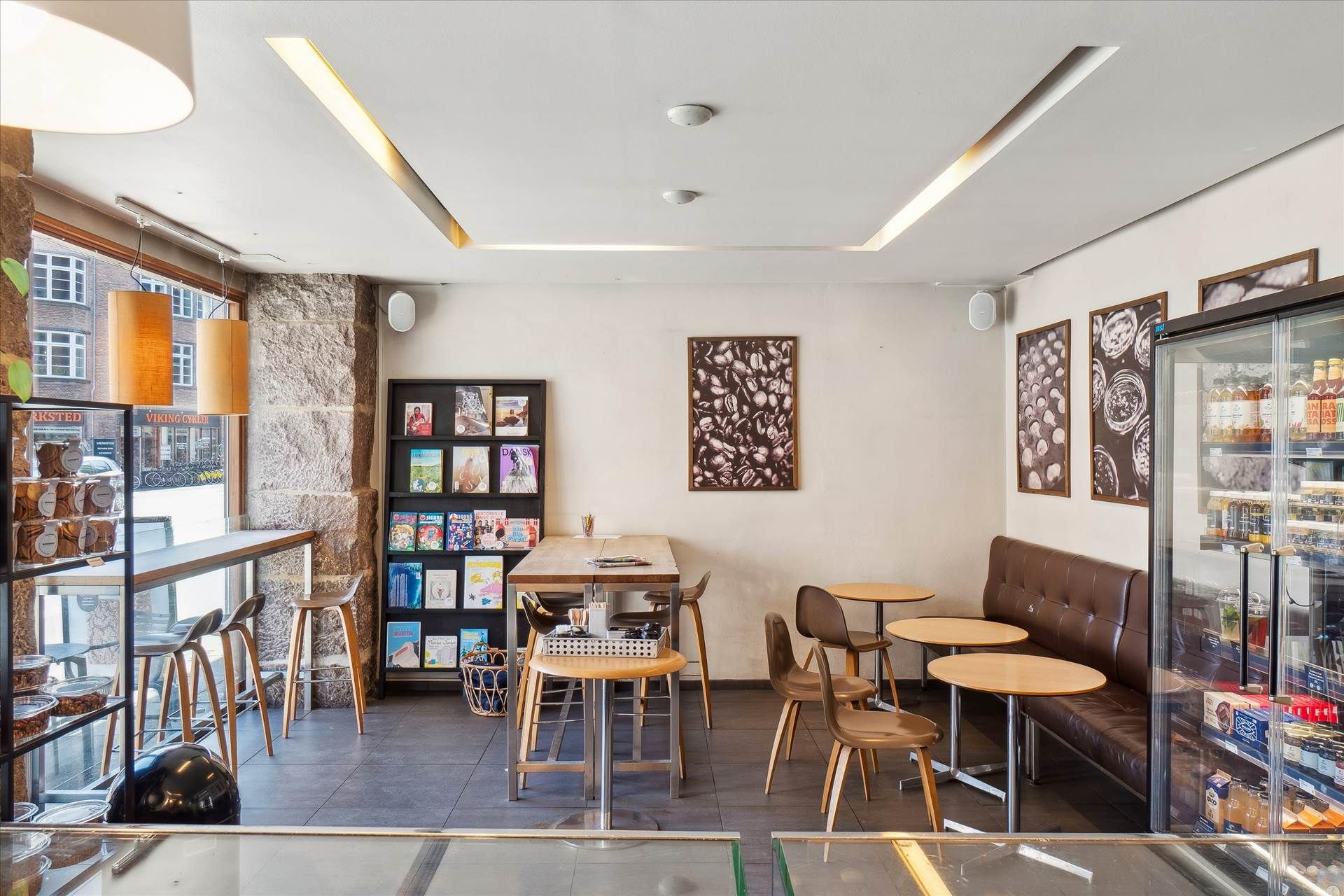 En moderne og veludstyret café med stolpeborde og stole samt et køleskab fyldt med snacks og drikkevarer