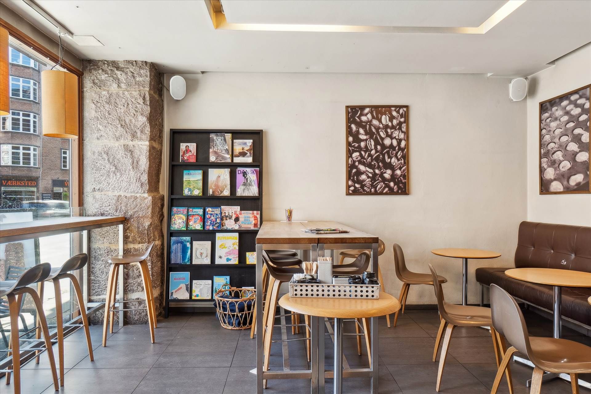 En hyggelig café med træborde, stole og en lænestol ved en glasvæg med byudsigt