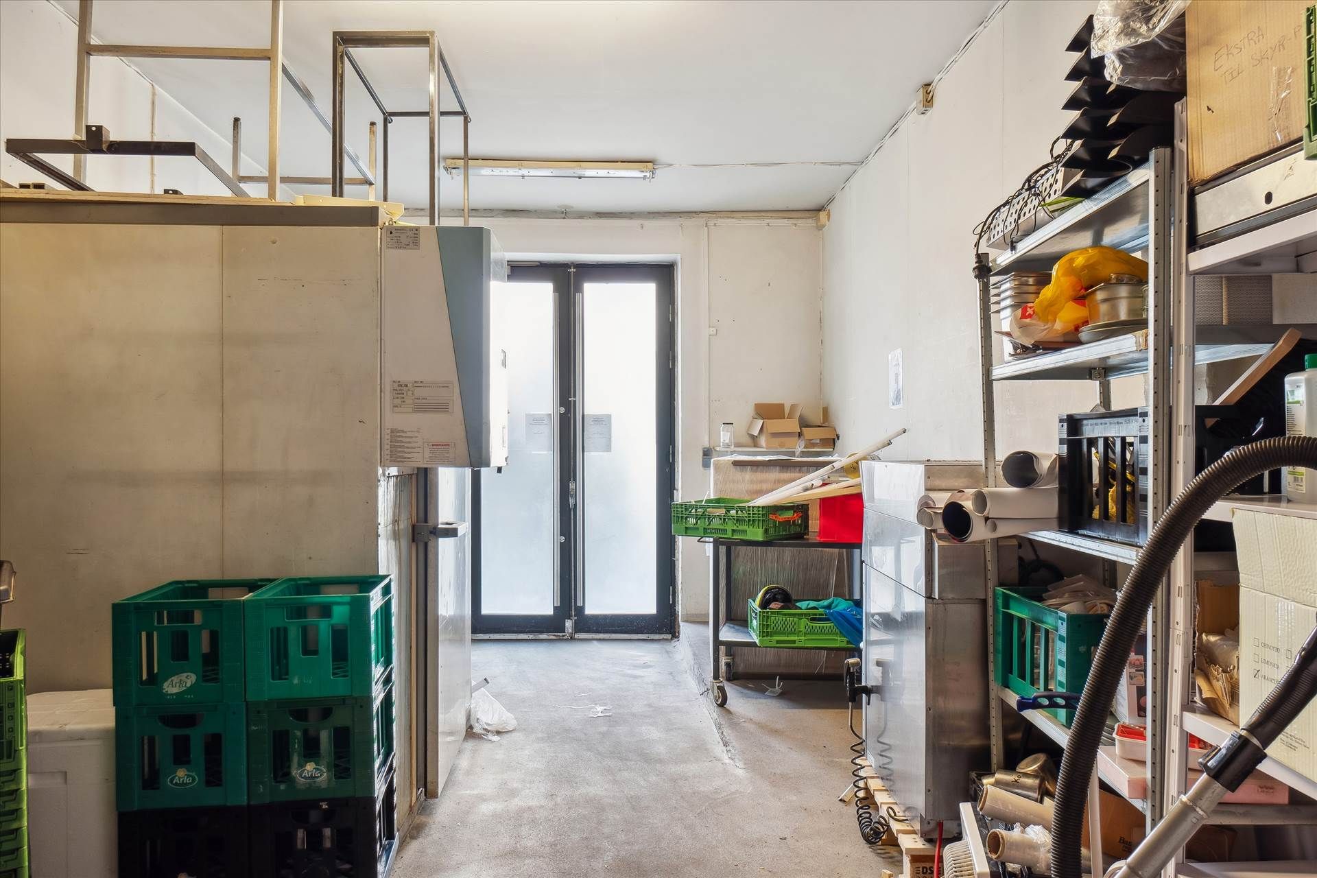 Lager med store hvide plastkasser og køleskabe samt stående hylder med kasser og kartoner.