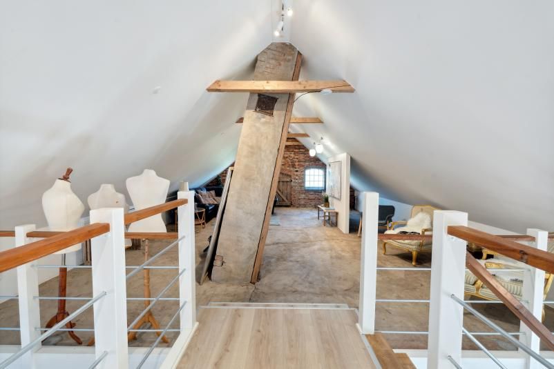 Et husloft med loftsvinduer og søjler, hvor der er tøjfigurer og møbler i loftet, samt en høj søjle og lysekroner