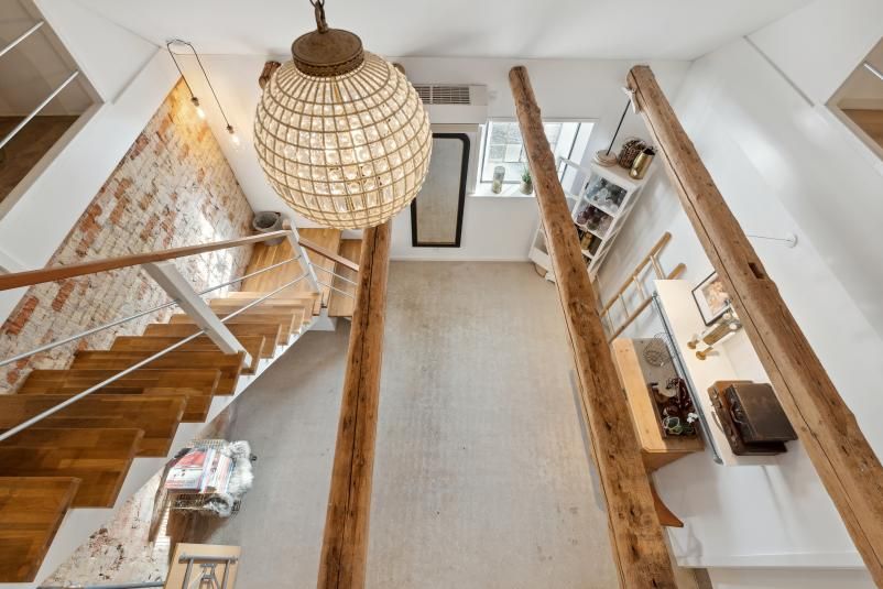 Indvends stue med lyse loft, åben gulvplan og lysekroner i loftet, der reflekterer sollys fra vinduet