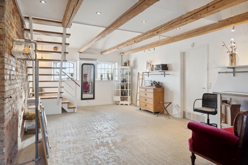 Værelse med højt loft og træbjælker, lysegul gulv og loft, rødt sæde, bord og stol, træskab, spejl og lysekroner