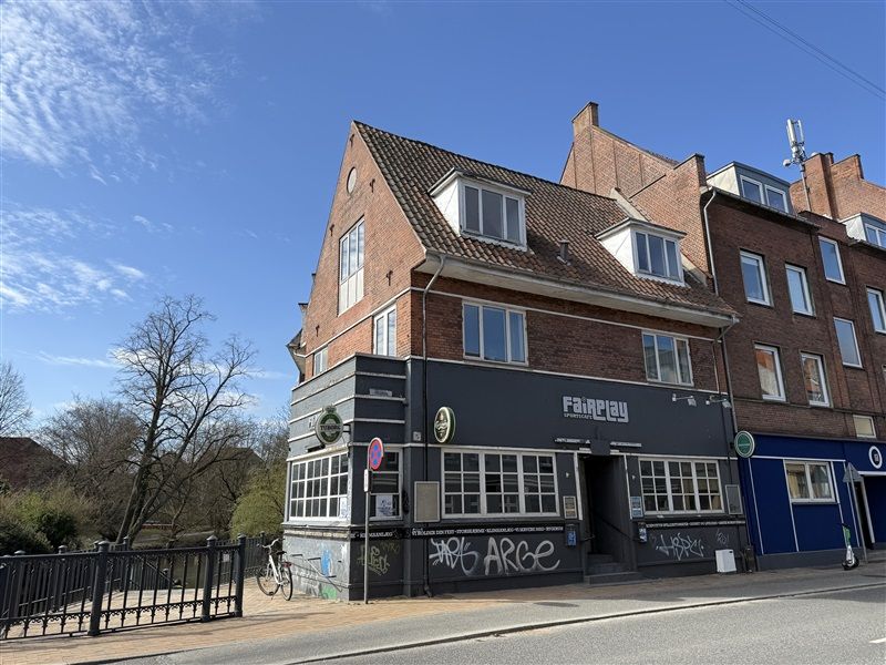 Brogade 5 i Odense med et skråt tag og facaden med graffiti og teksten Fairplay. Der er et cykelstativ foran og en gågade