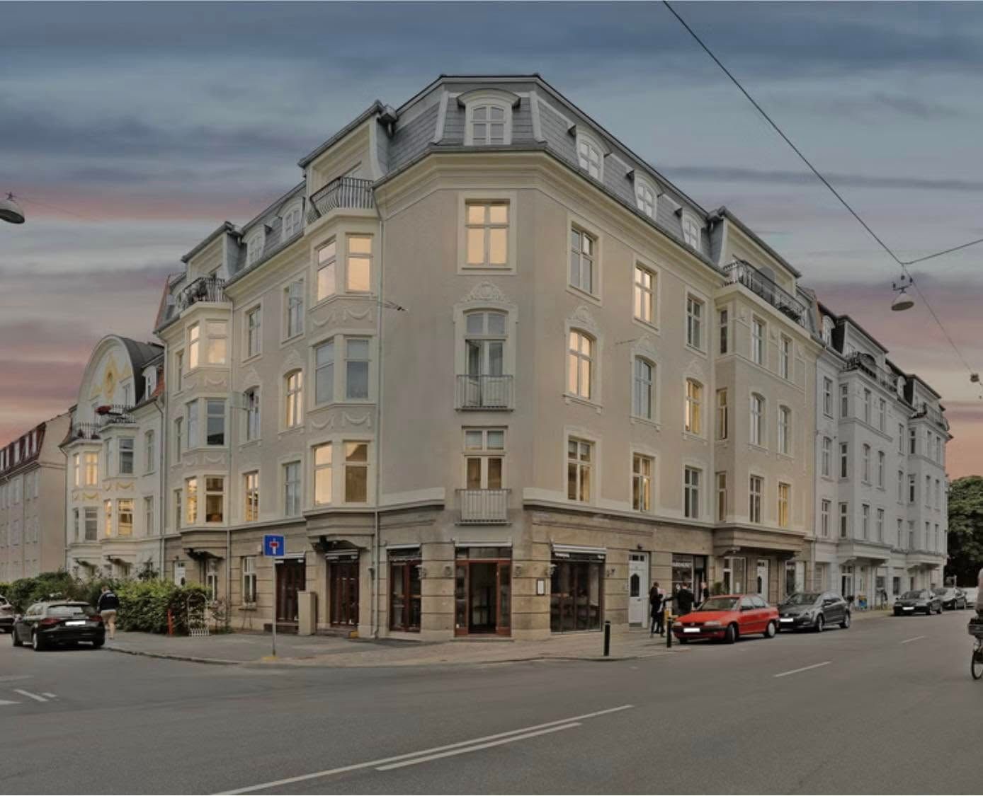 Erhvervslejemål på Frederiksberg C. Moderne bygning med store vinduer og lyse interiører. Et par biler kører langs gaden og