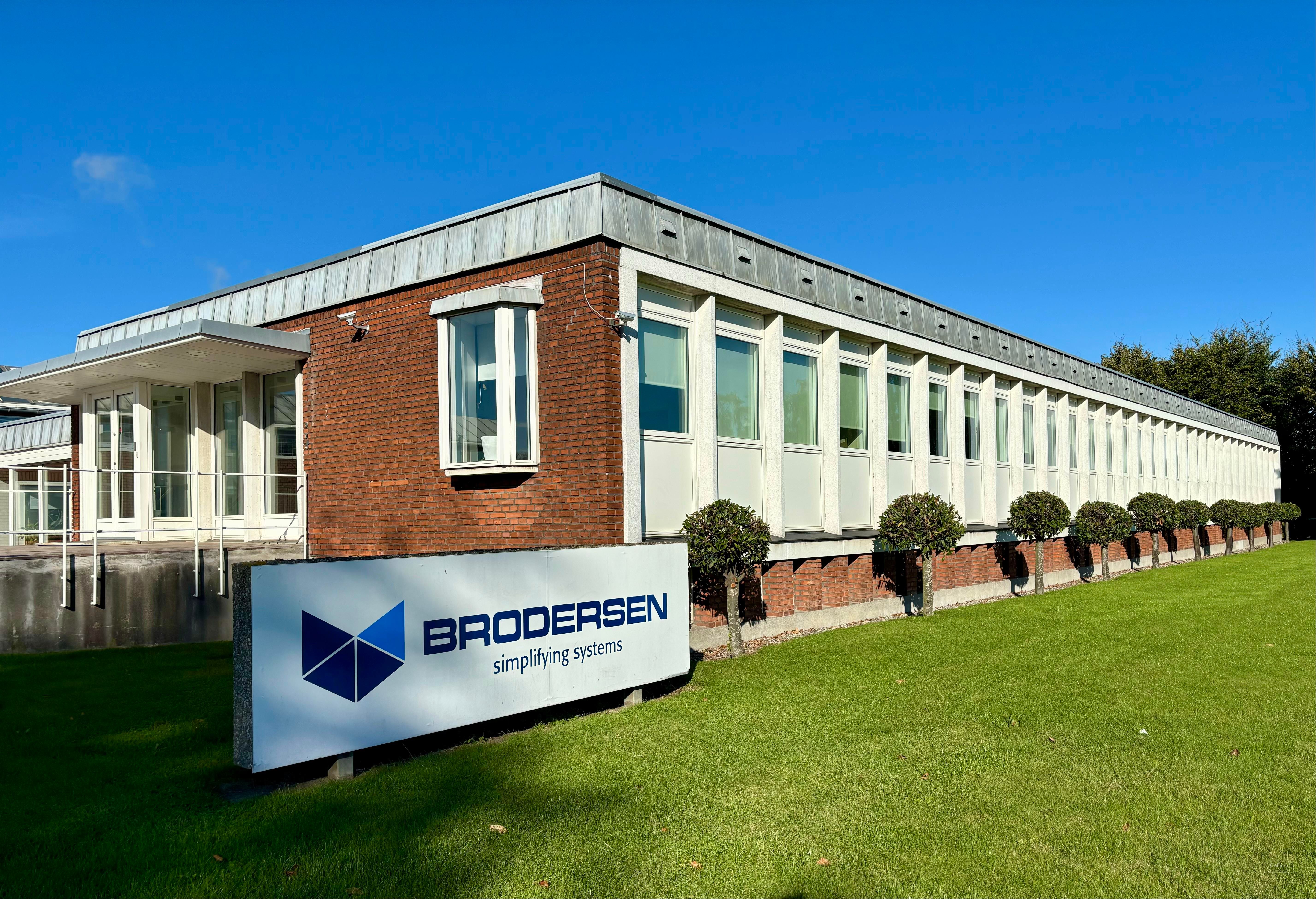 Store bygning med røde mursten og hvide vindueskarm og teksten Brodersen Simplifying Systems på skiltet foran