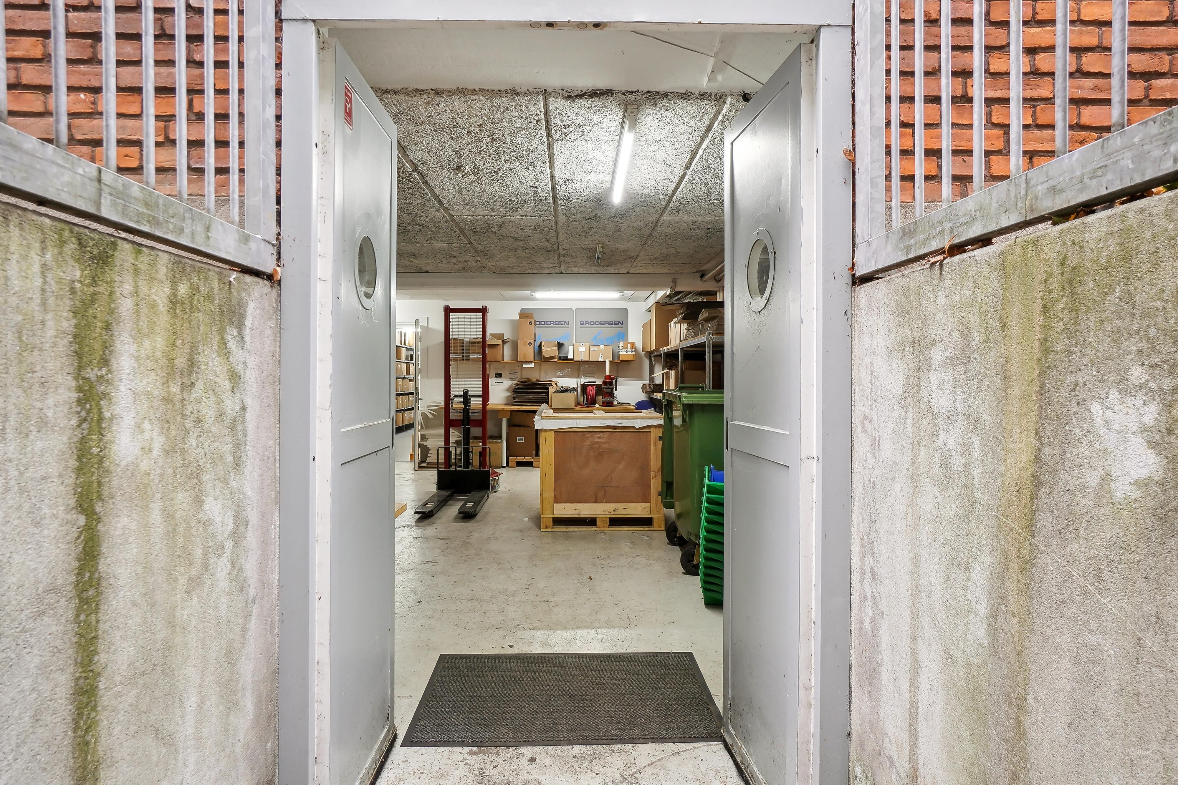 Lager med åbne døre, indvendige lagerhylder og et stort vinduesskud, som ser ud i et lager med en række trækasser og to