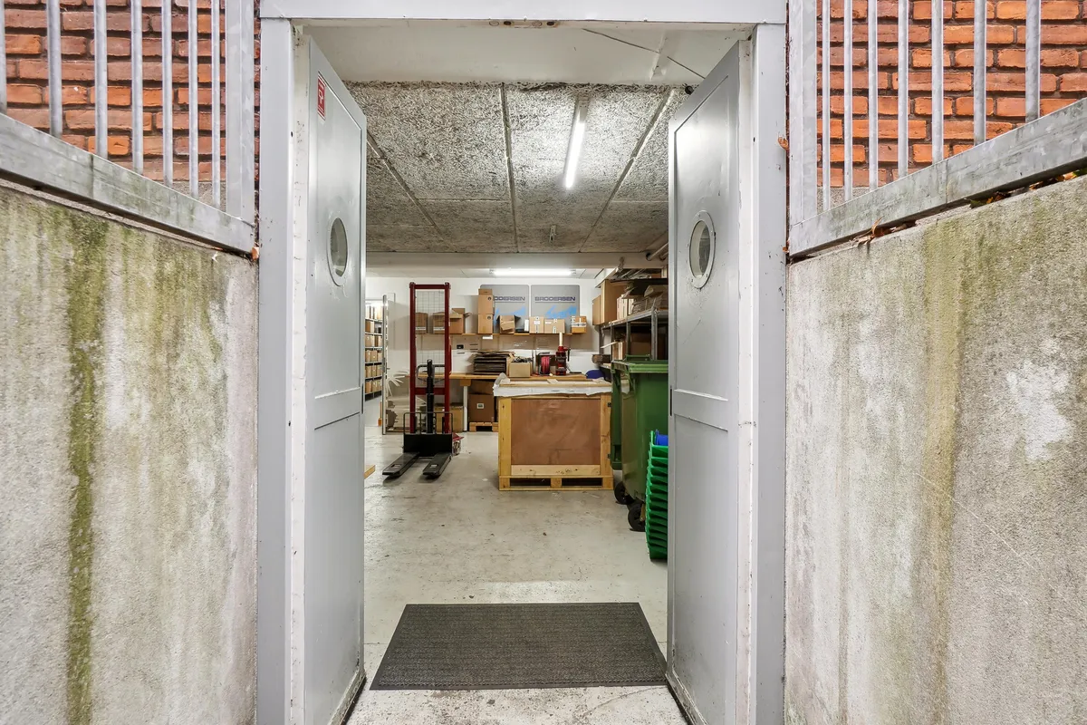 Lager med åbne døre, indvendige lagerhylder og et stort vinduesskud, som ser ud i et lager med en række trækasser og to