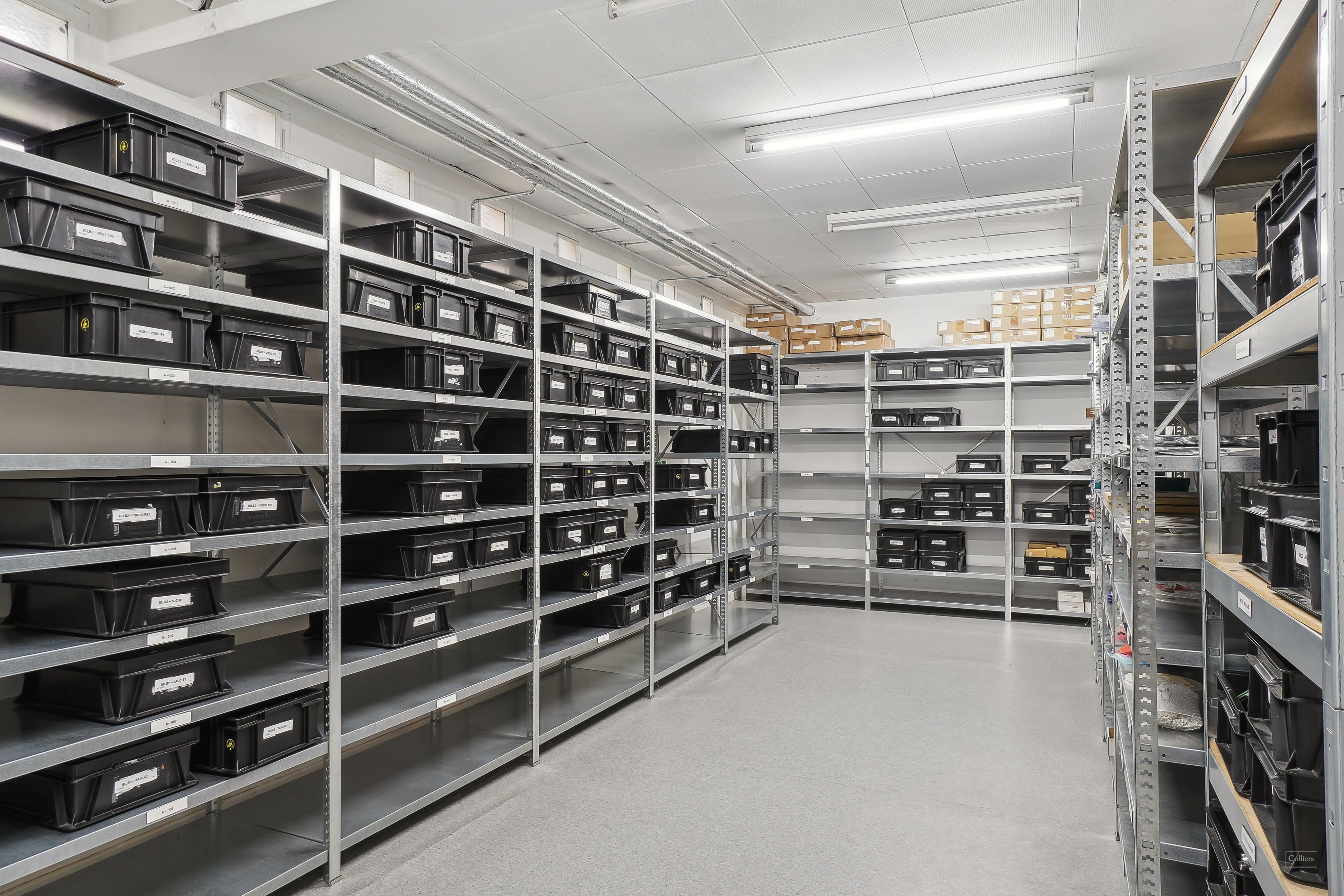 Lager med flere metalhylder, hver med sorte kasselagre, højt til loftet og godt oplyst af hvide loftslamper