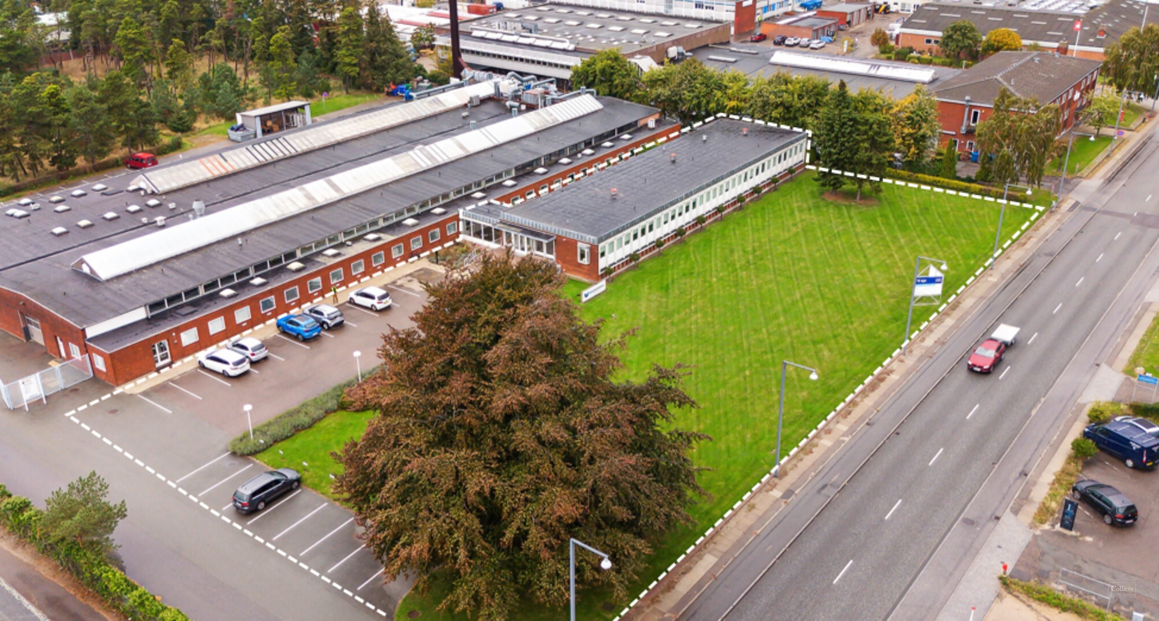 Kortlægning af et bygningsområde med lager og parkeringspladser, to biler kører på vejen og tre parkerede biler