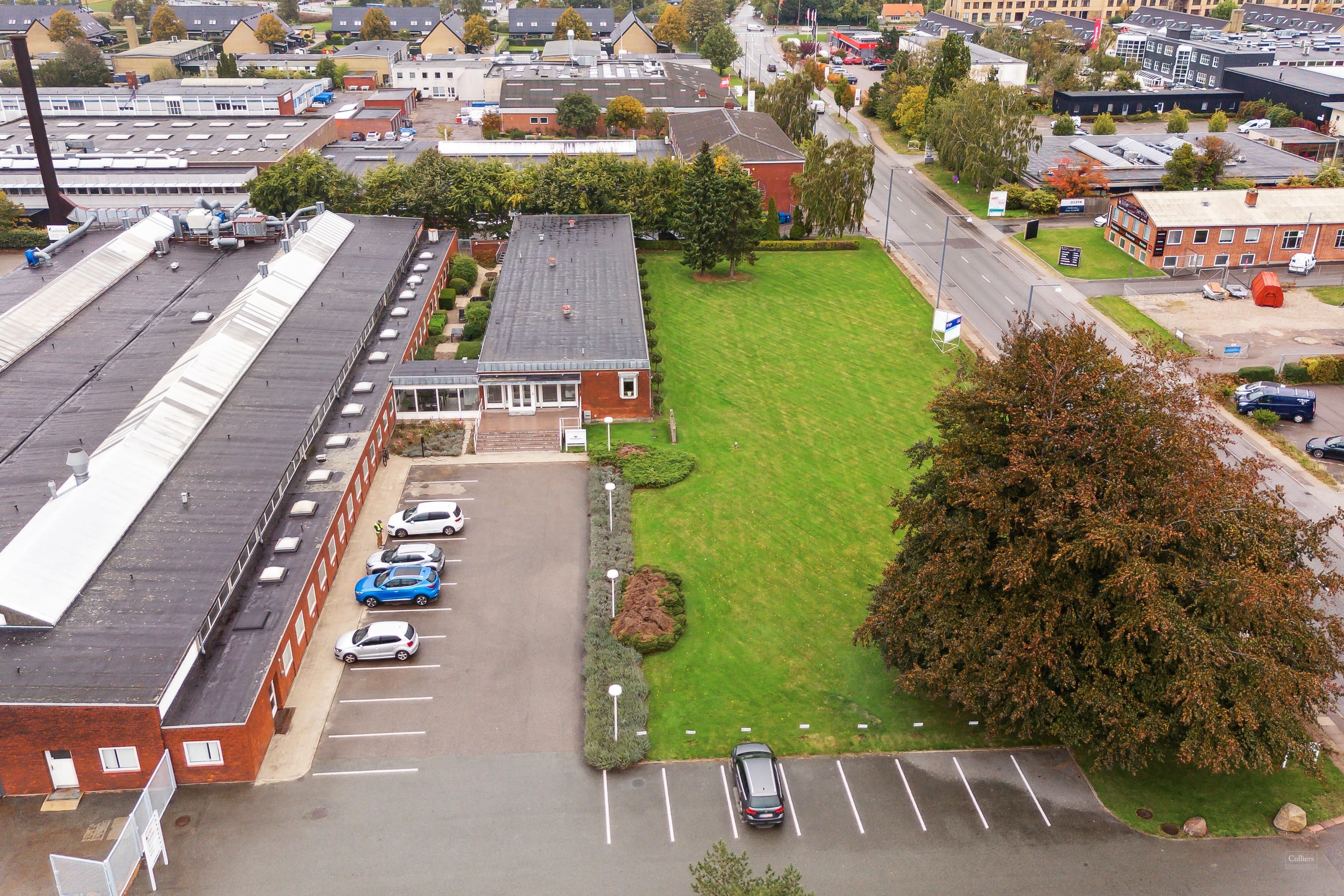 Et parkeringsområde med flere parkerede biler og en grøn plæne med træer og buske