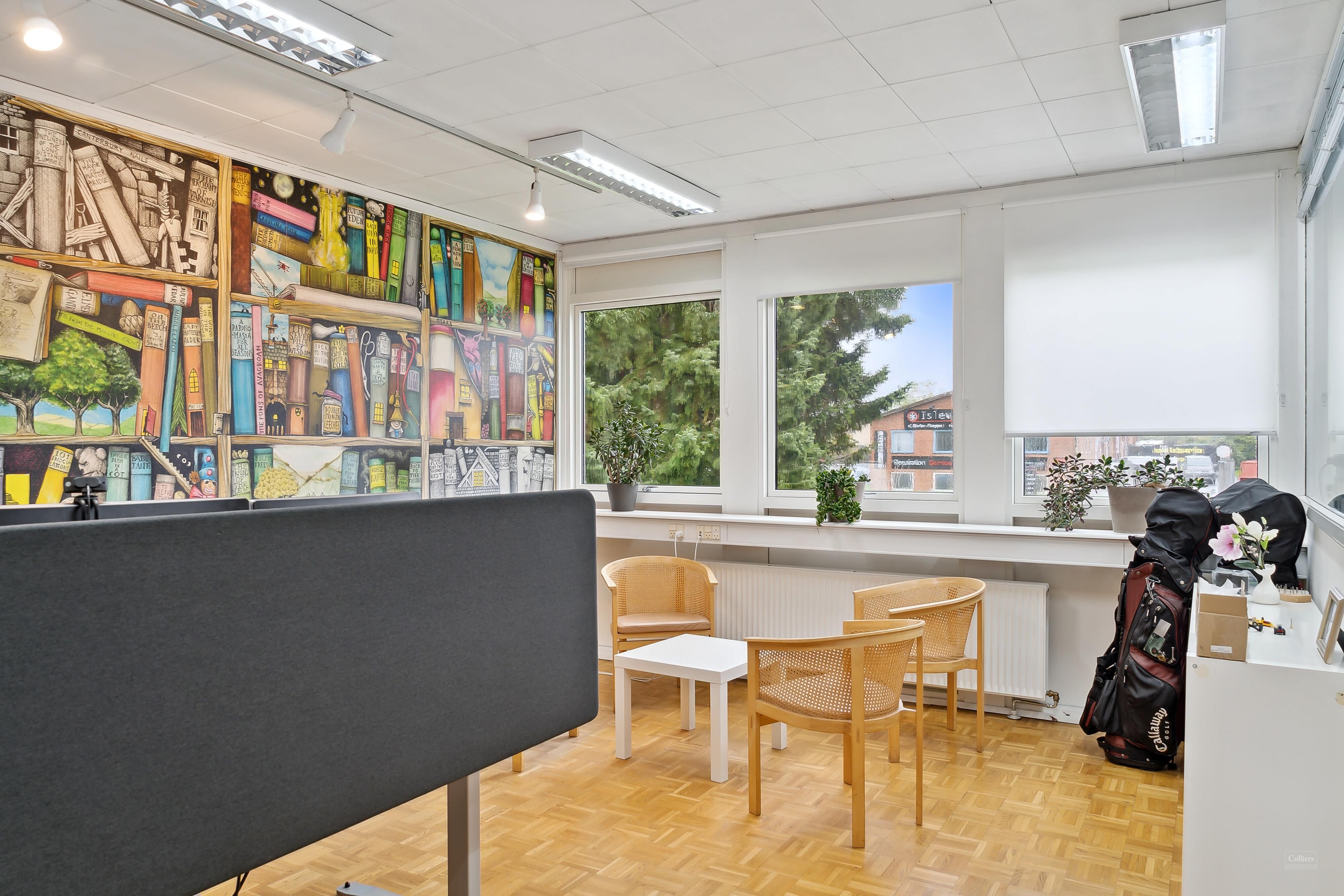 Kontorrum med bøger på væggen, bord og stole, golfkuffert og blomster og lysekroner på loftet