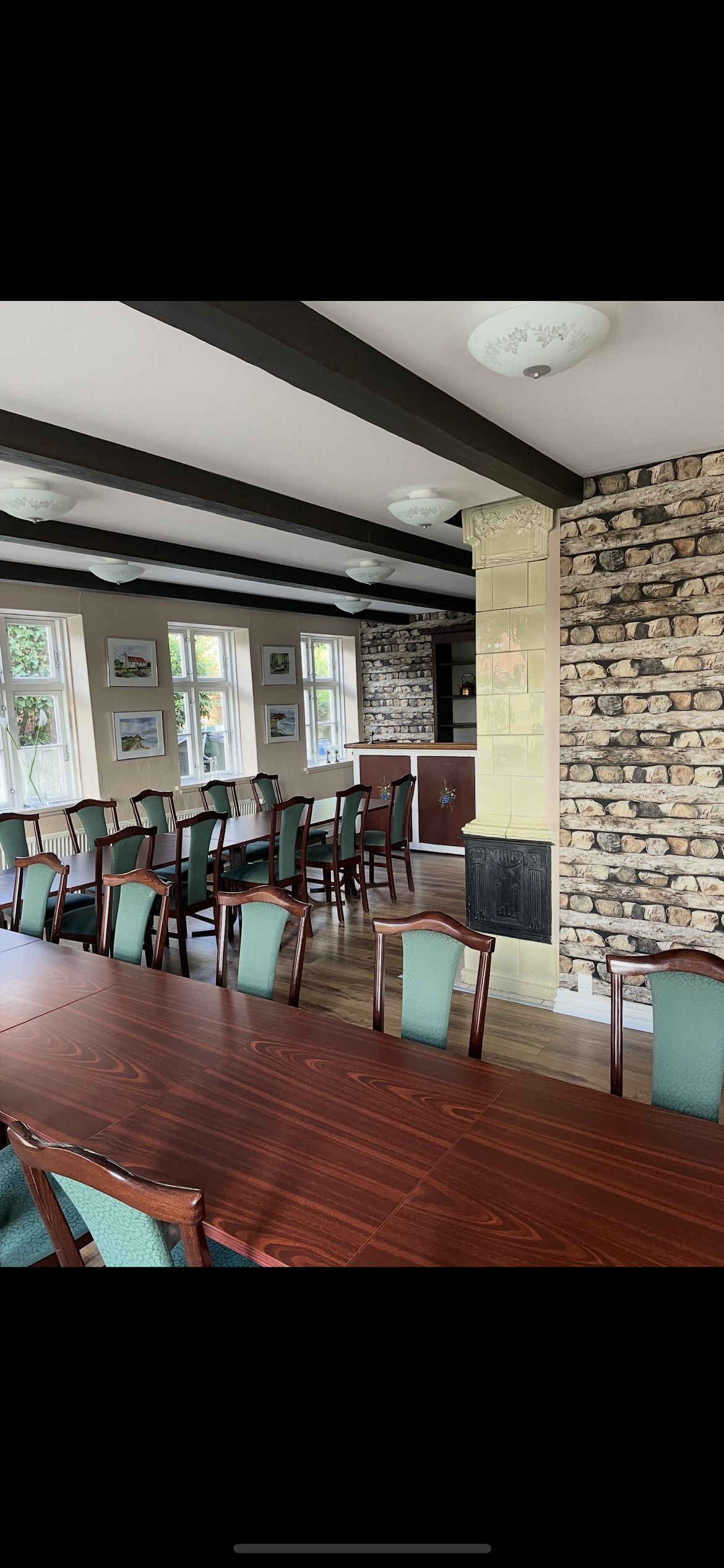 En stor lyse stue med lyse lofter og lysekroner, en åben ildpejs og træborde med grønne stole