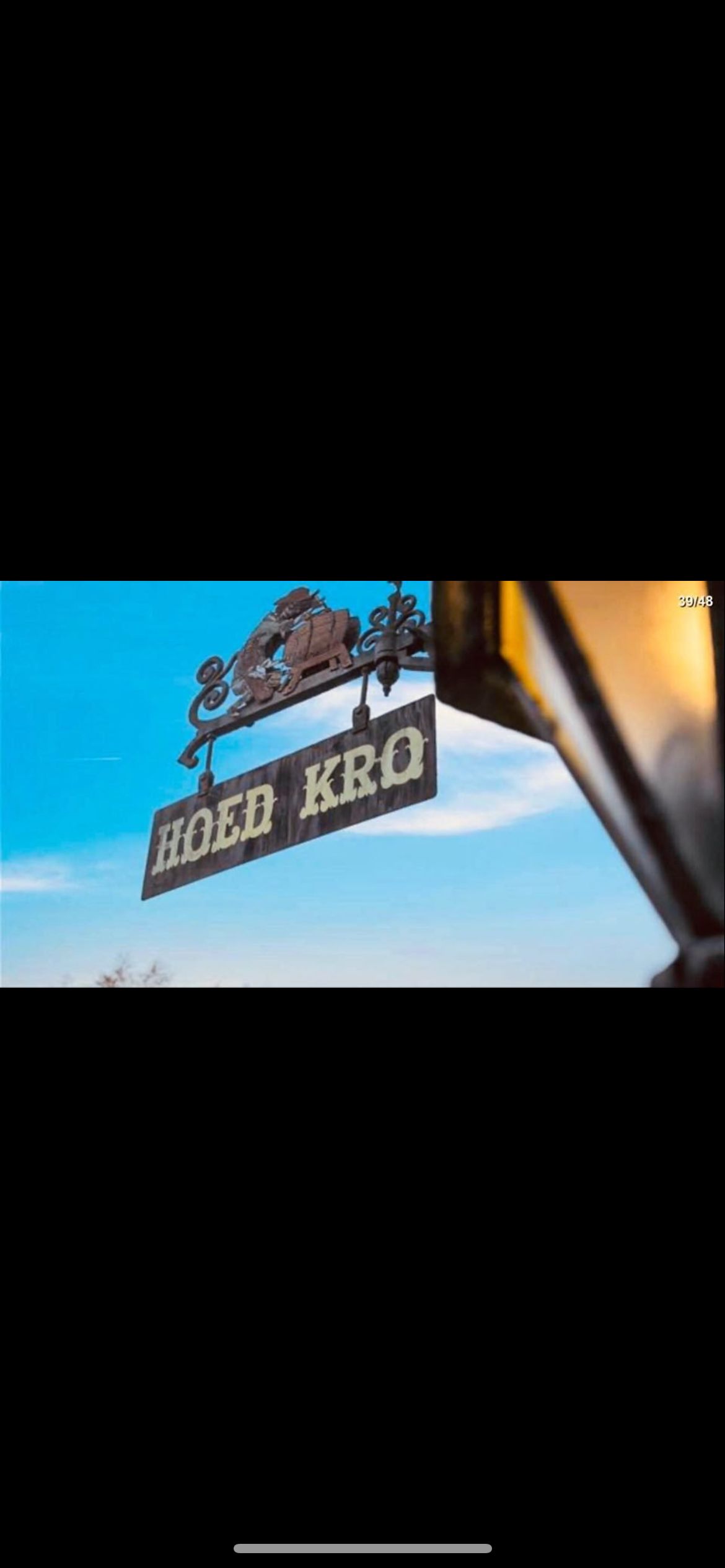 Foto af en skov med et skjold med navnet Hoed Kro og datoen 39/48, placeret i et landskab med blå himmel og hvide skyer